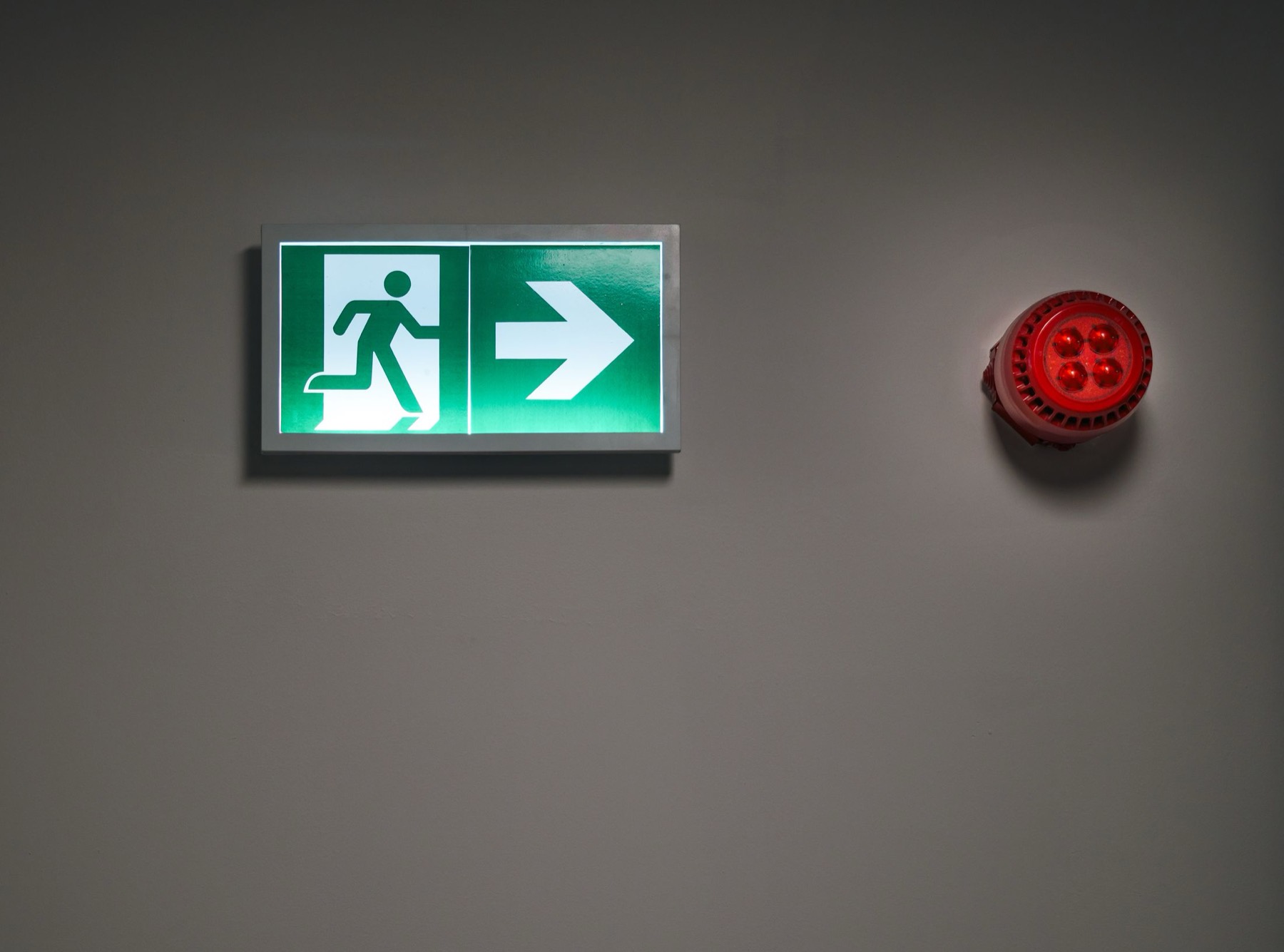 An illuminated emergency exit sign and sounder on a wall