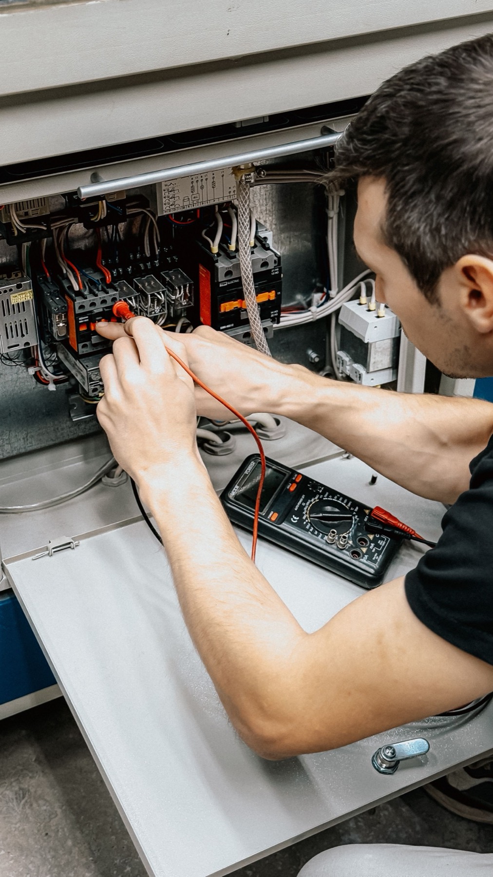 An electrician testing connections inside a panel with a multimeter