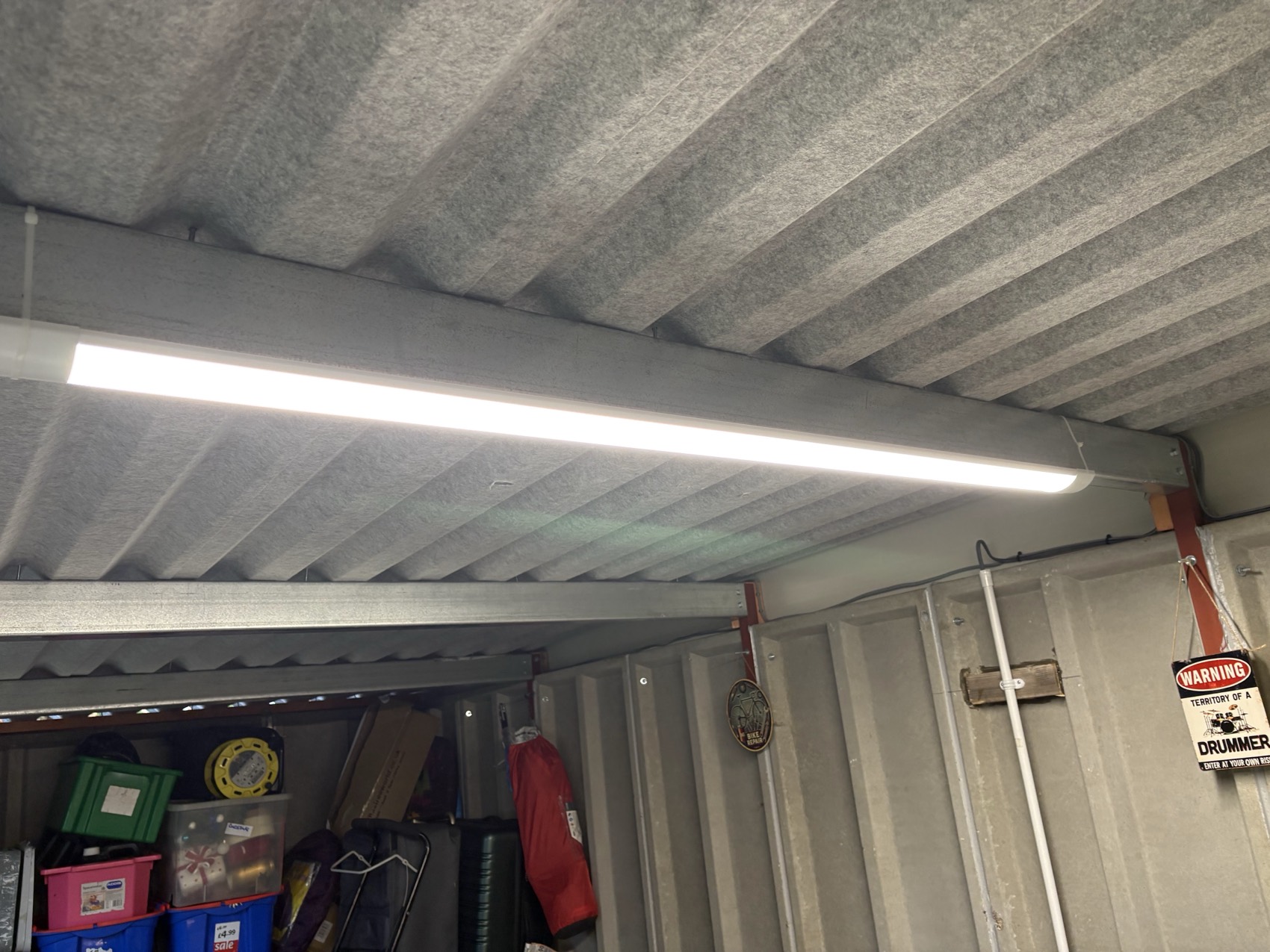 LED batten lighting in a steel outbuilding — surface fixed to the structure with the supply run on the ceiling line, so a garage full of boxes is finally usable.